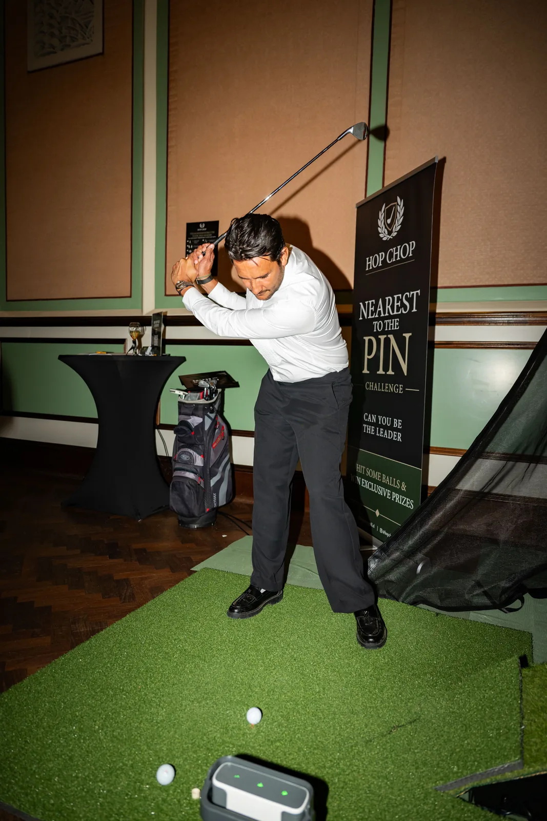 Gast in wit overhemd haalt uit op de afslagmat naast de Nearest to the Pin banner