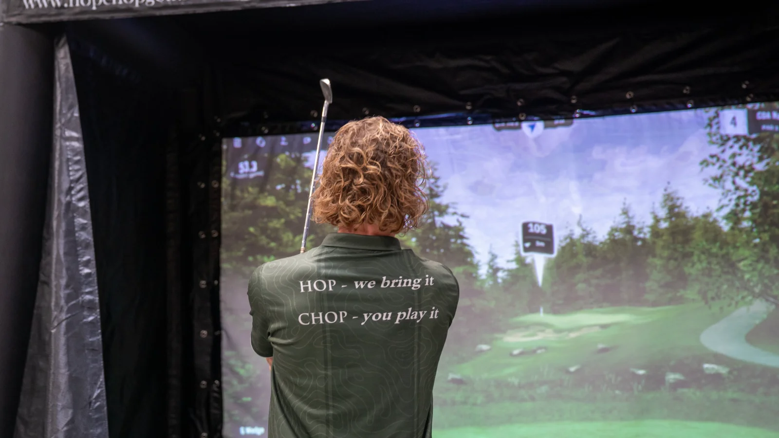 Golfer in HOP CHOP shirt met de tekst we bring it, you play it voor het simulatorscherm