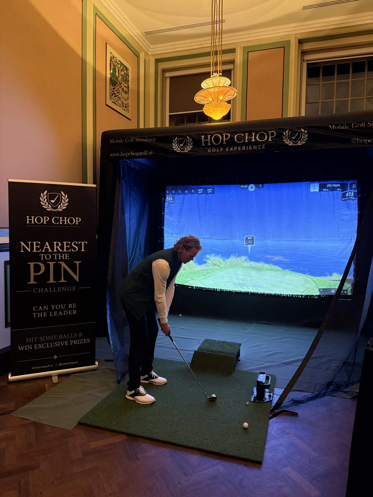 Golfer in groene bodywarmer slaat af in de HOP CHOP simulator naast de Nearest to the Pin banner
